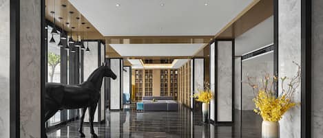 Un hall d’hôtel moderne avec un sol en marbre poli, une statue de cheval et un vase rempli de fleurs jaunes.