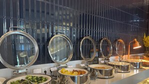 A buffet setup with multiple stainless steel serving dishes and a modern, reflective wall in the background. - Paco Hotel Guangzhou Baiyun Airport Liantang Metro (Guangzhou)