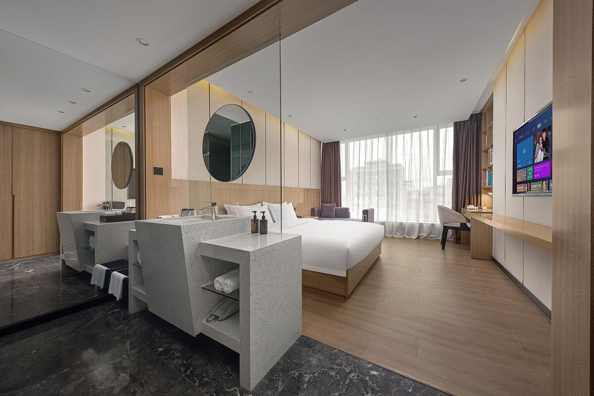Una habitación de hotel moderna con una cama grande, un área de estar, un tocador con espejo y un televisor.