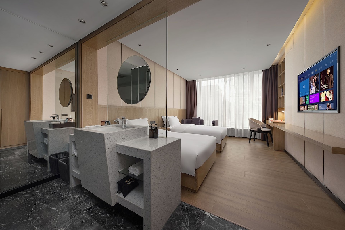 Habitación de hotel con cama, escritorio, tocador con espejo y televisión en la pared.