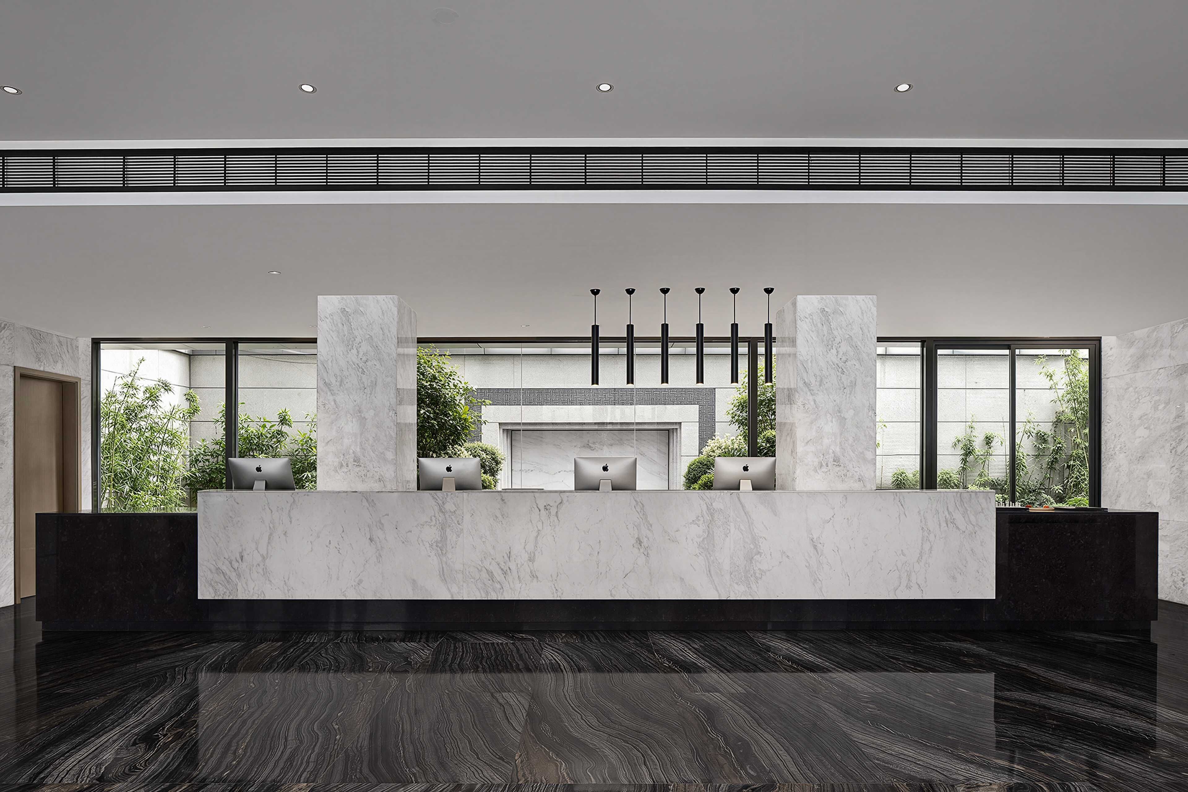 A modern reception area with a marble counter, multiple computer stations, and large windows offering views of greenery.