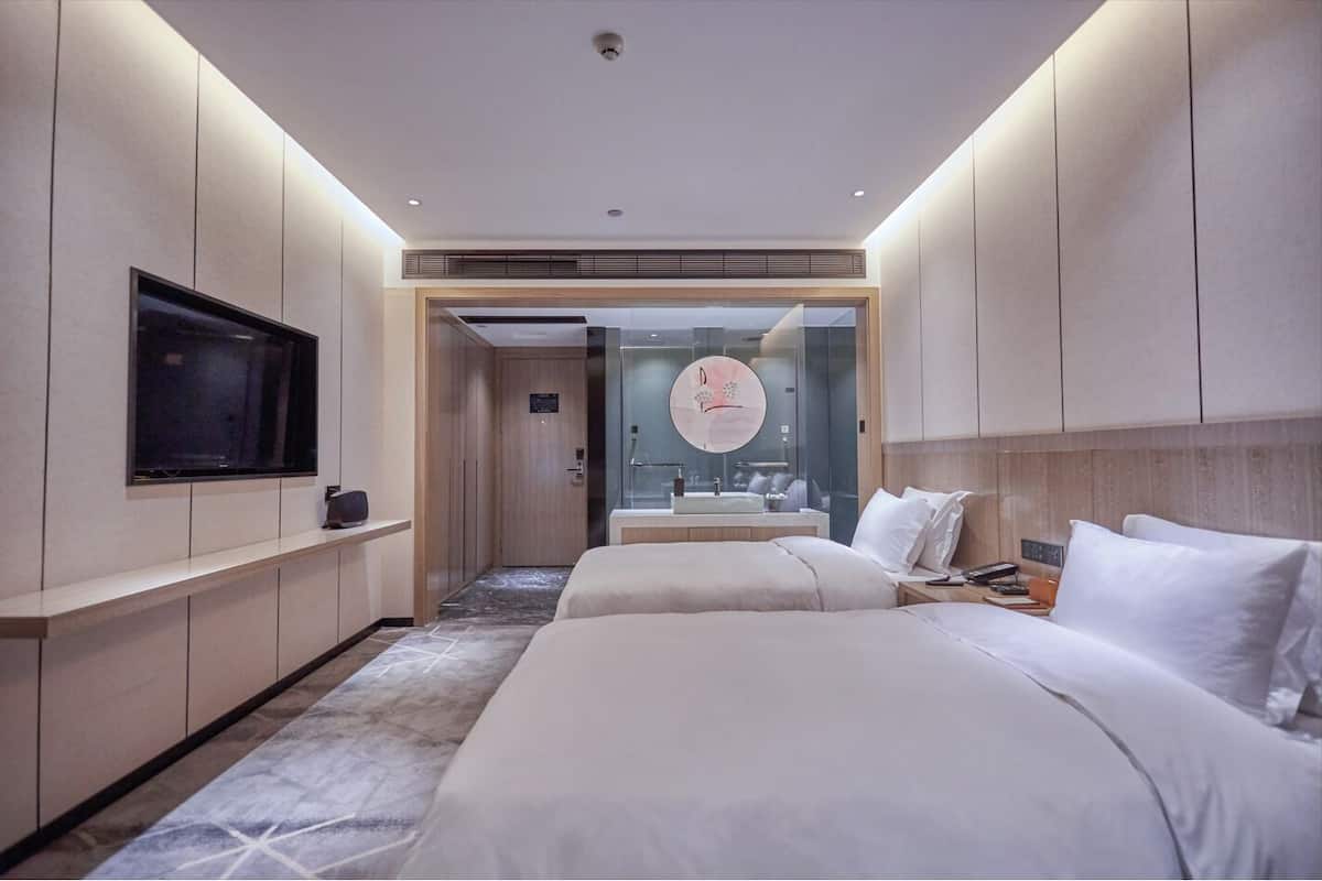 Una habitación de hotel moderna con una cama grande, un televisor montado en la pared, un baño con espejo y un pasillo que conduce a otra habitación.
