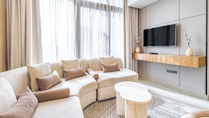 A modern living room with a sectional sofa, a flat-screen TV mounted on a wooden shelf, and a patterned rug. - Superhost Modern 1BR in Azizi Riviera (Dubai)