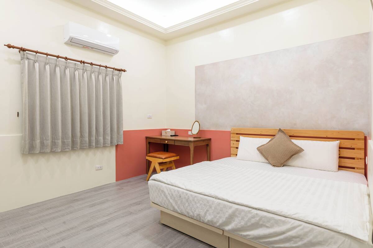 A bedroom with a bed, a desk, a chair, an air conditioner, and a curtain.