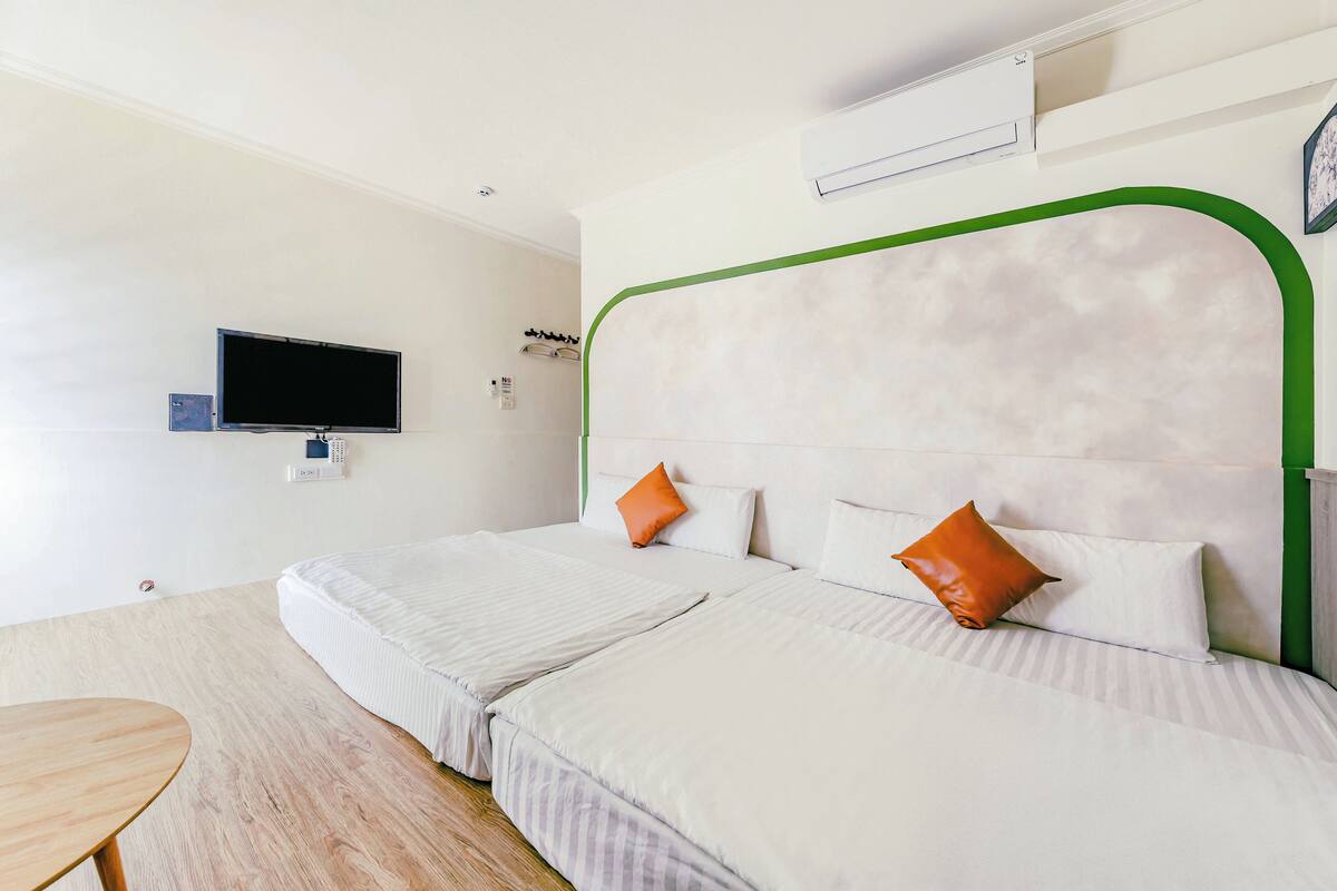 A hotel room with two beds, a television, an air conditioning unit, and a small table.