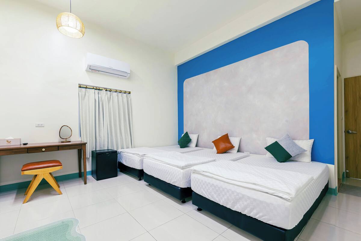 A hotel room with two beds, a desk, a chair, an air conditioner, and a large window.