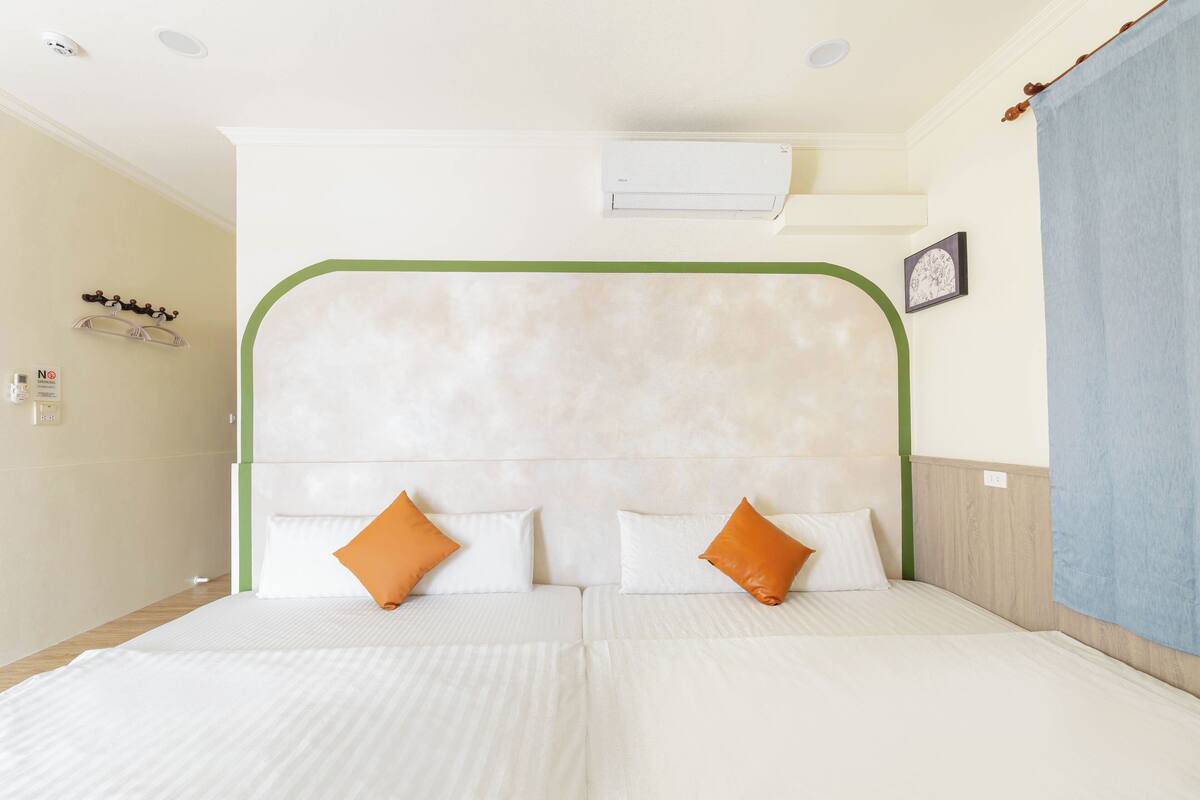 A double bed with a green headboard, two pillows, a wall-mounted air conditioner, and a picture frame.