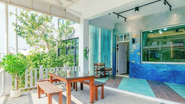 A covered outdoor seating area with a table and benches, a potted plant, and a view of a building with a blue wall and a window. - Mugang Retreat｜Liuqiu Kids' Playroom (Liuqiu)