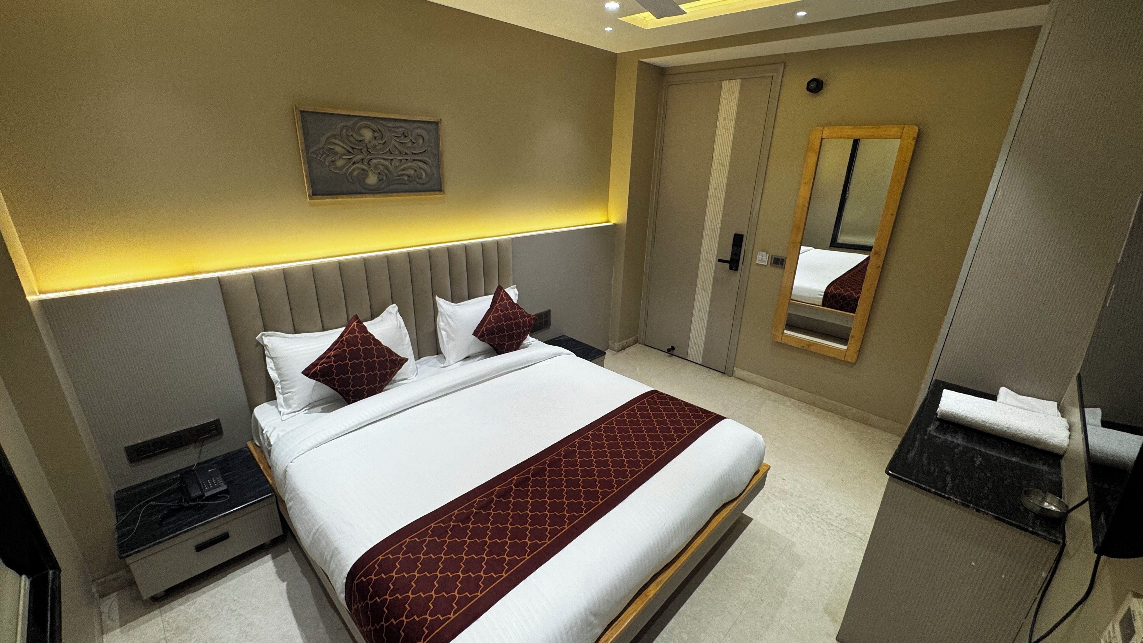 A modern hotel room with a large bed, a bedside table, a mirror, and a wall-mounted artwork.
