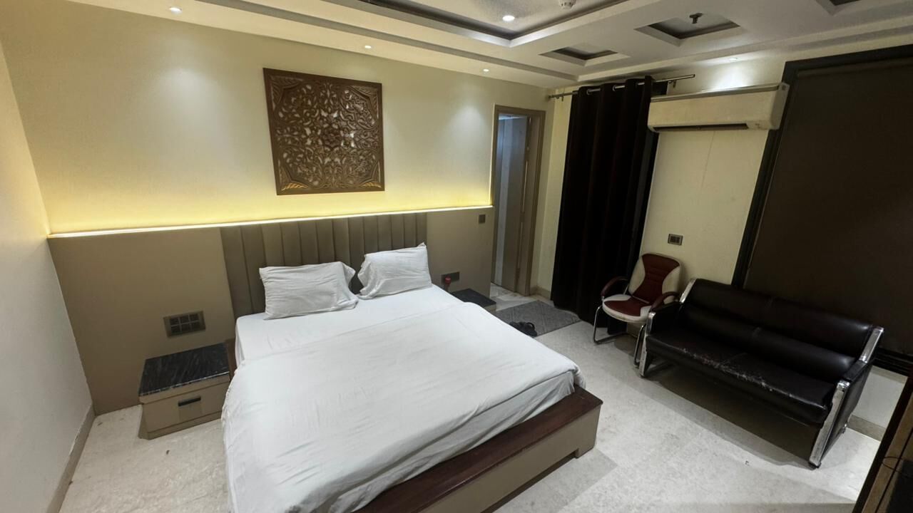 A modern hotel room with a large bed, a desk, a chair, and a bench.