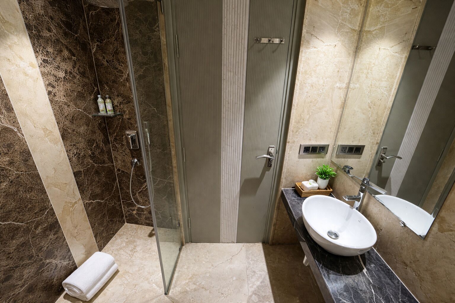 Une salle de bain moderne avec une douche à parois de verre, un meuble-lavabo avec un évier blanc et des murs en marbre.