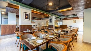 Ein Restaurant mit mehreren Esstischen und Stühlen, Holzdetails und gerahmten Bildern an den Wänden.