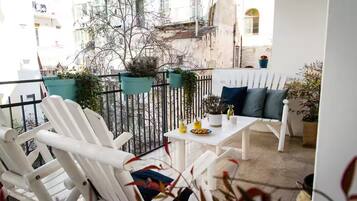 A balcony with white chairs and a table, potted plants, and a view of buildings and a river.