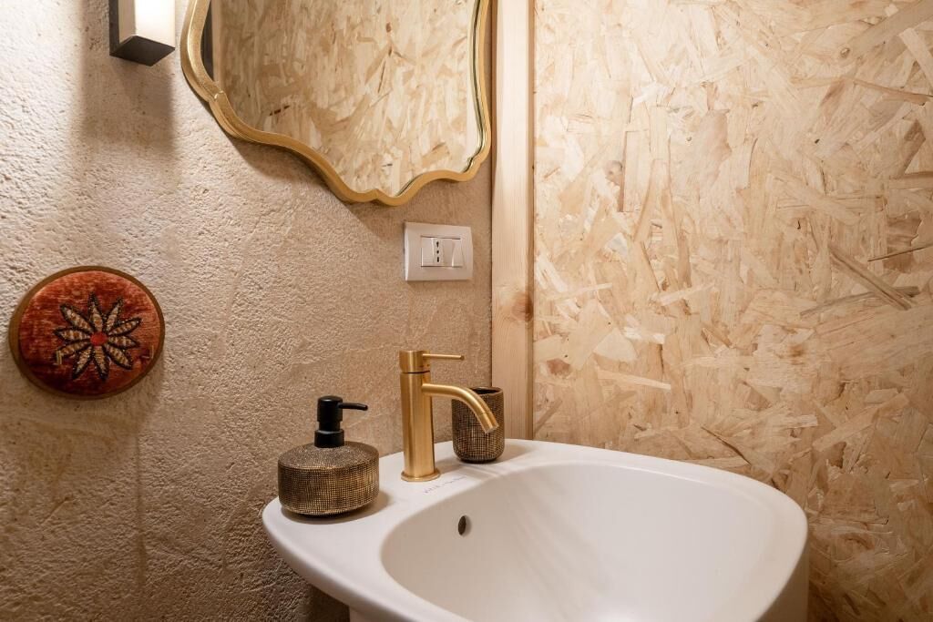 A bathroom with a white sink, gold faucet, and a round soap dispenser.