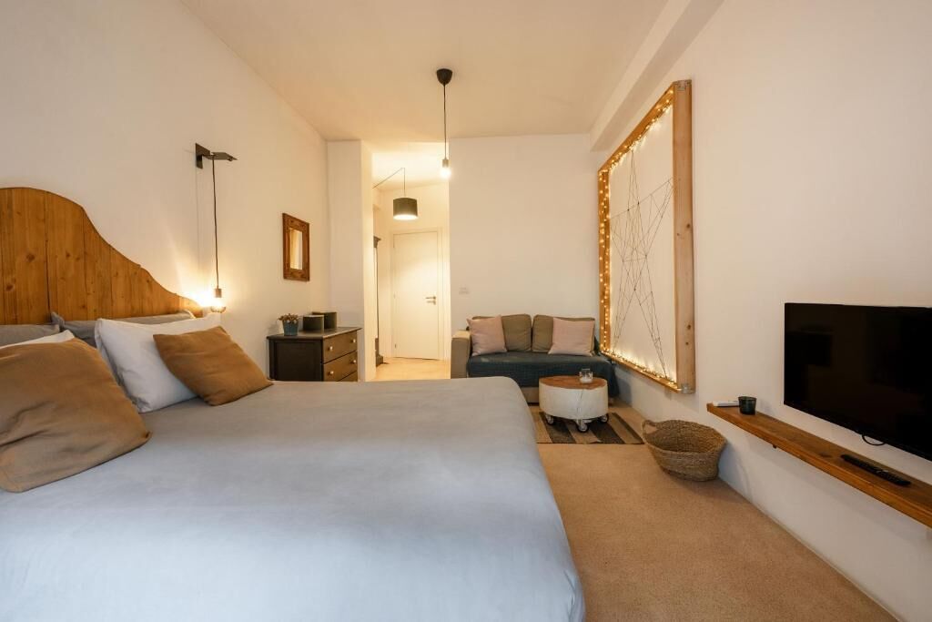 Un dormitorio con una cama grande, televisión, cabecero de madera, sofá y espejo con luces.