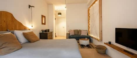 Un dormitorio con una cama grande, televisión, cabecero de madera, sofá y espejo con luces.