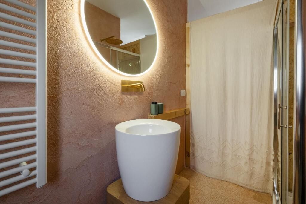 Un bagno con un lavandino bianco grande, uno specchio rotondo con illuminazione integrata e una tenda da doccia.