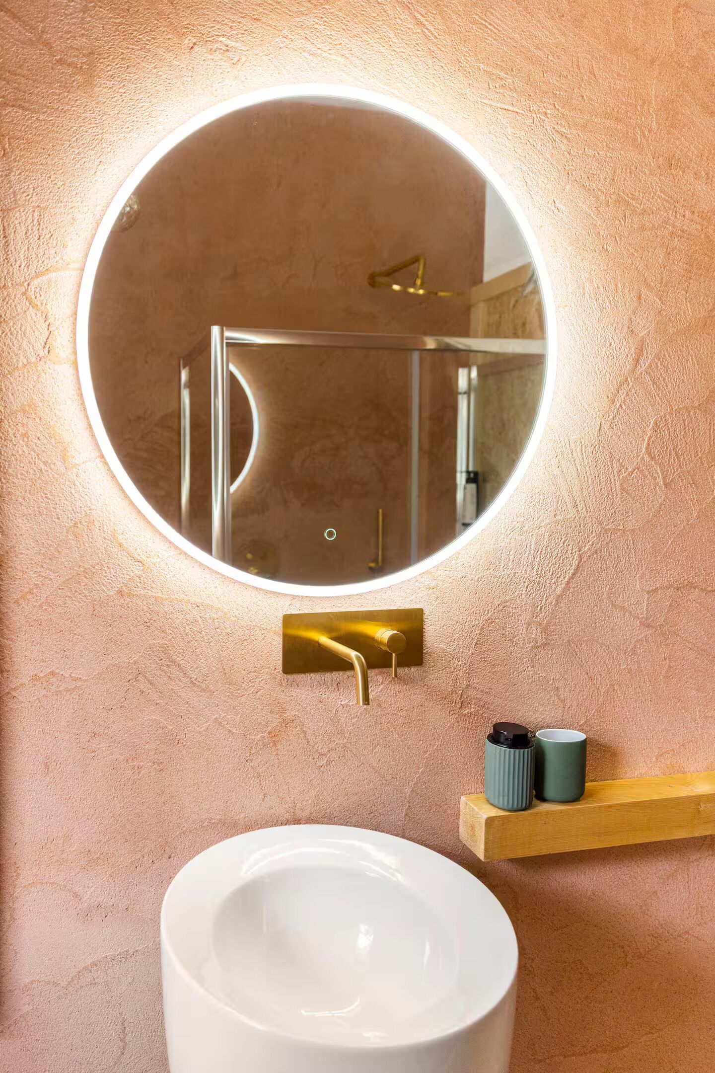 Un bagno con uno specchio rotondo, un lavandino bianco e uno scaffale in legno con due tazze.