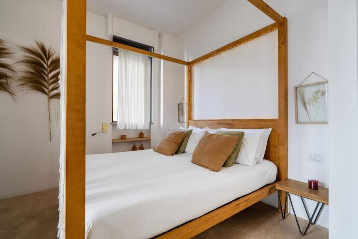 A four-poster bed with a wooden frame, white bedding, and multiple pillows.