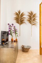 Una stanza con una scrivania in cemento, due fiori viola in vasi marroni, un cesto intrecciato e un elemento decorativo a parete.