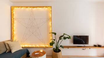Ein modernes Wohnzimmer mit großem Wandbild, Fernseher, Sofa, Beistelltisch und Topfpflanze.