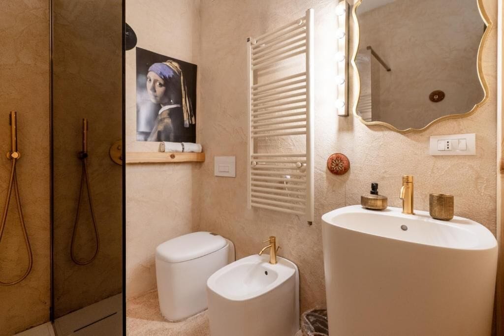 Une salle de bain avec un lavabo blanc, des toilettes, une douche et un miroir avec un cadre doré.