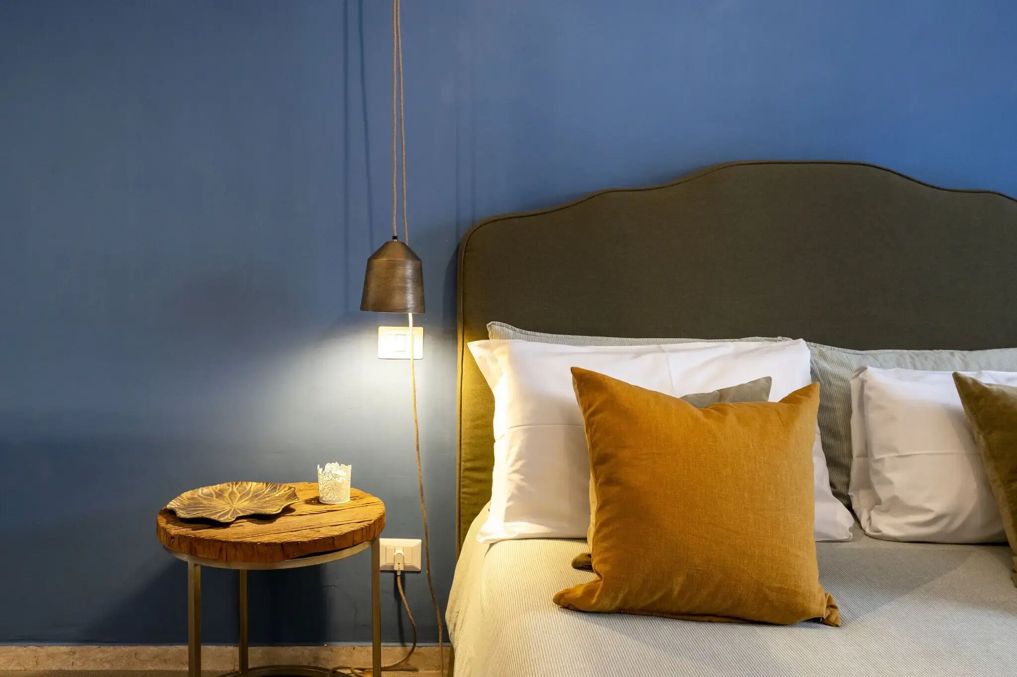 A neatly made bed with a headboard, a bedside table with a lamp, and a decorative leaf on the table.