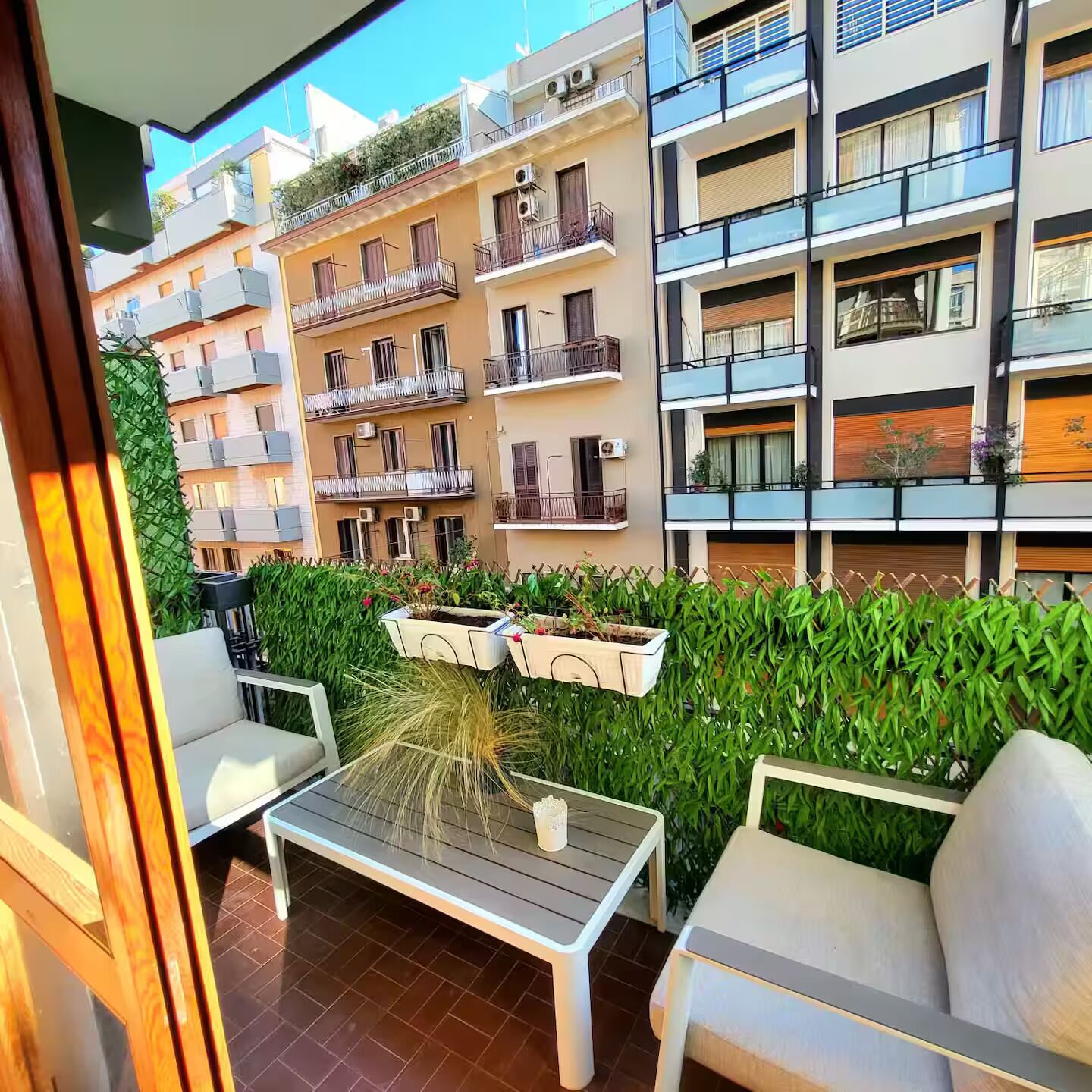 A balcony with a table and chairs, surrounded by a hedge and a row of balconies.