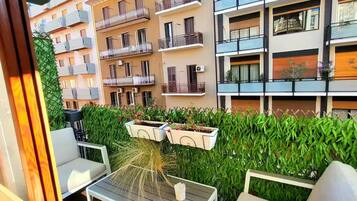 A balcony with a table and chairs, surrounded by a hedge and a row of balconies.