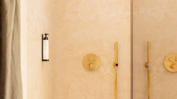 A bathroom with a beige textured wall, a shower with a golden showerhead, and a bottle of shampoo on the wall.