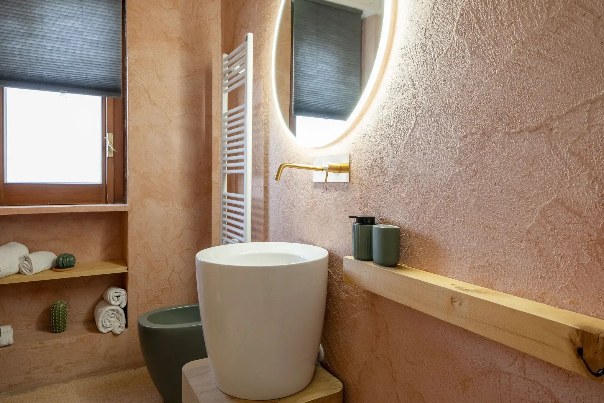 Un baño con un lavamanos grande de color blanco, un grifo dorado, un perchero y un estante con artículos de tocador.