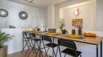 Una cuina moderna amb un taulell llarg, cadires negres i diferents objectes de cuina.