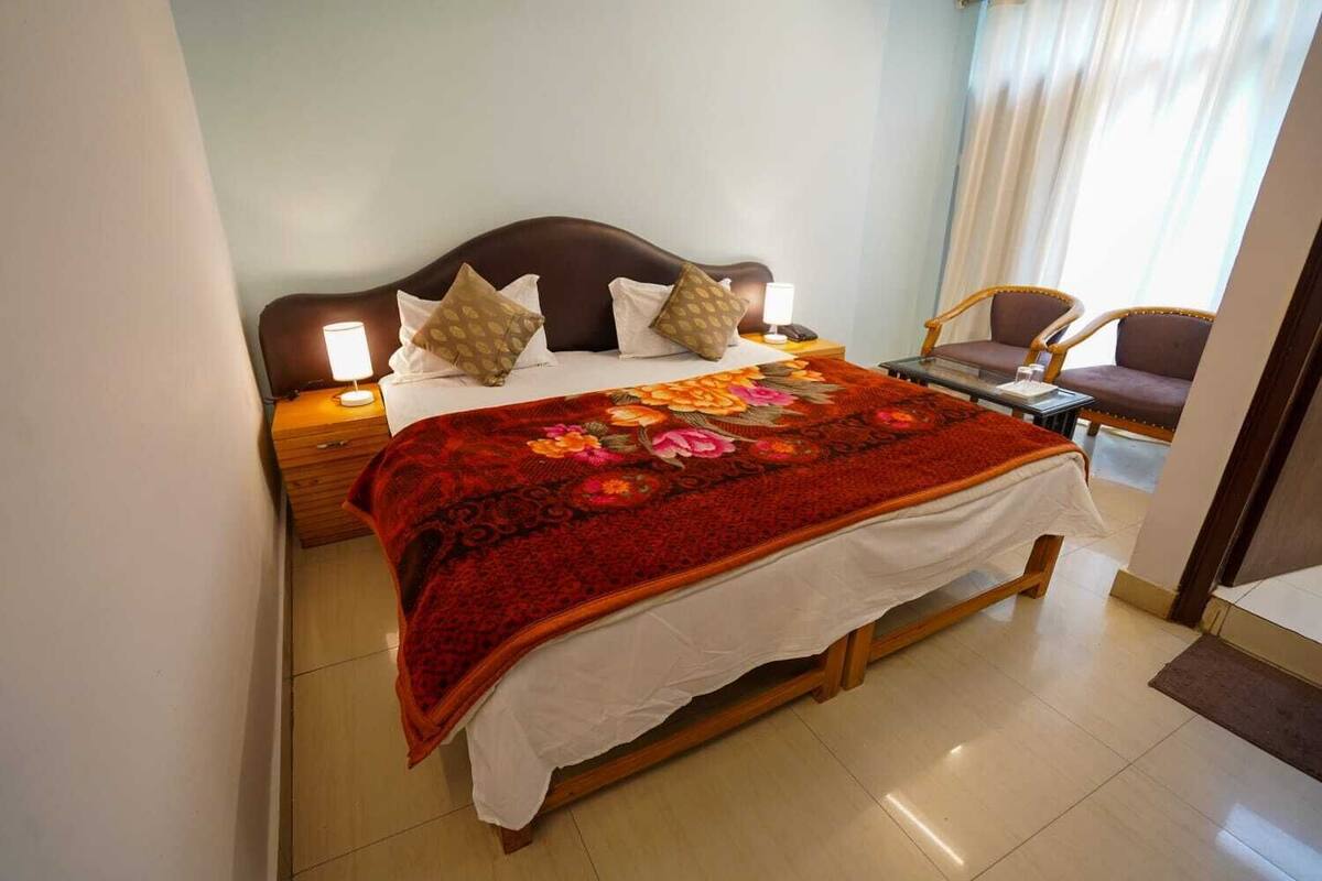 Un lit bien fait, recouvert d’une couvre-lit à motifs floraux, avec deux lampes de chevet et une chaise, dans une pièce bien éclairée dont le sol est carrelé.