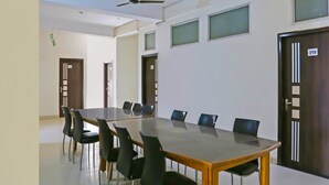 A conference room with a long table, black chairs, and a ceiling fan. - Super Hotel O The Star Guest House (Rewari)