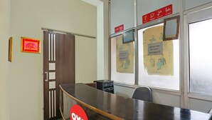 A reception desk with a red logo, a wooden door, and a window with informational posters. - Super Hotel O The Star Guest House (Rewari)