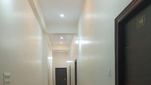 Un pasillo con una puerta oscura a la derecha, una pared de color claro e iluminación empotrada en el techo.