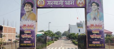 A gate with a signboard displaying text in a non-English script, flanked by two pillars with images and text.
