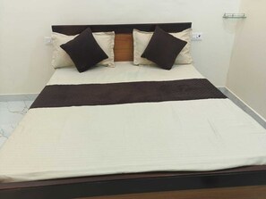 A bed with a wooden headboard, two pillows, and a white and brown bedspread. - Hotel Pampa Sarovar (Rajnagar)
