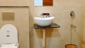 A bathroom with a white toilet, a white sink, a mirror, and a shower. - Hotel Babylon Elegance (Mathura)