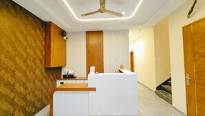 A reception area with a modern design, featuring a reception desk, a ceiling fan, and a patterned wall. - Hotel Babylon Elegance (Mathura)