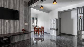 A modern living room with a marble floor, a flat-screen TV mounted on the wall, a dining area with a table and chairs, and pendant lighting.