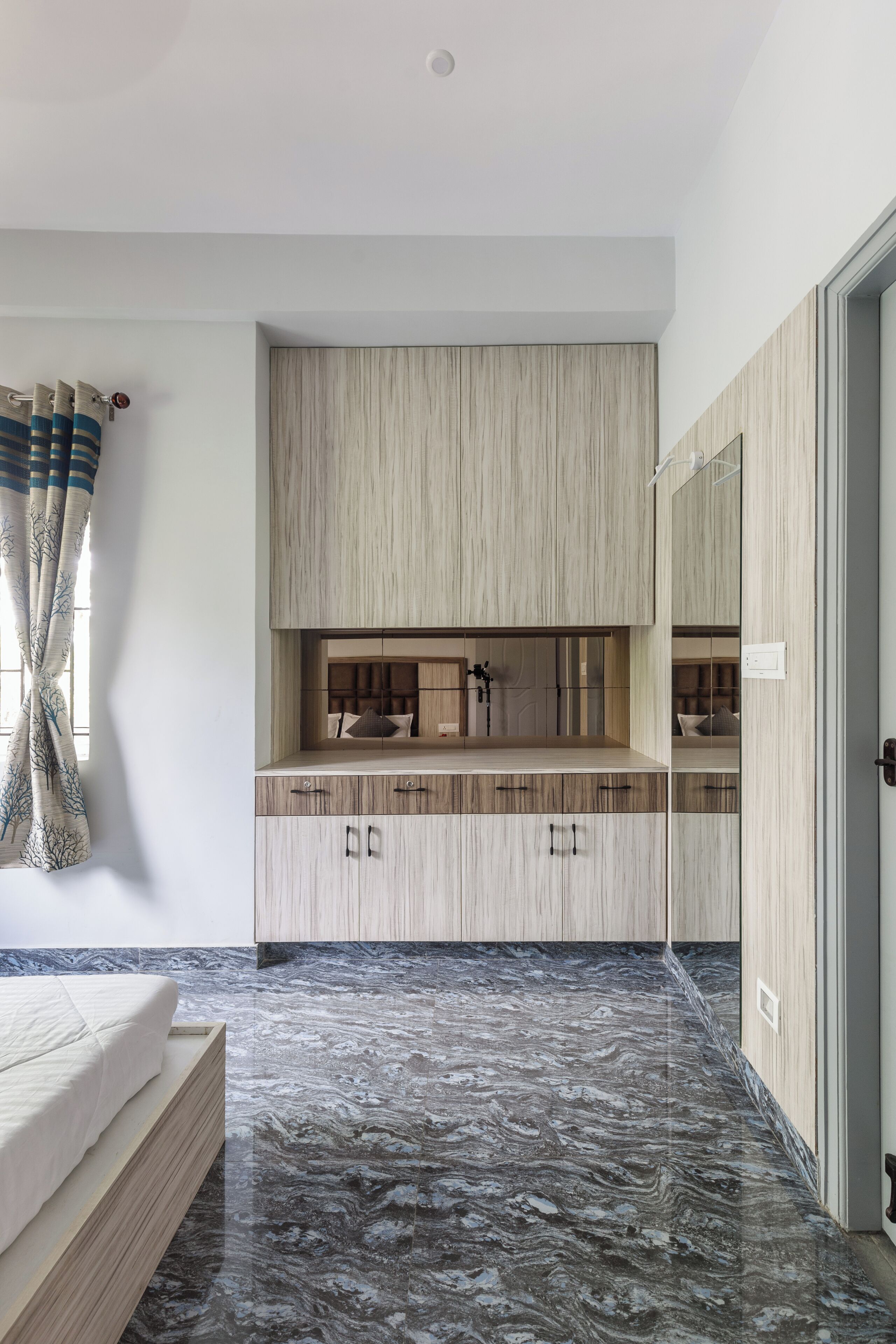 A modern bedroom with a bed, a marble floor, wooden cabinets, and a large mirror.