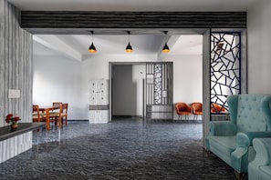 A modern living room with a marble floor, a teal sofa, and a dining area with wooden chairs and a table. - Indigo Studio by Jadecaps 1bhk New Town Kolkata (Barasat)