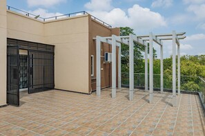 A rooftop terrace with a tiled floor, a black gate, and a white pergola structure. - Indigo Studio by Jadecaps 1bhk New Town Kolkata (Barasat)