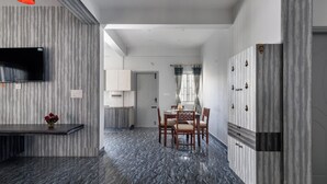 Una cocina moderna con televisión de pantalla plana, un comedor con mesa y sillas, y un pasillo que lleva a un dormitorio.