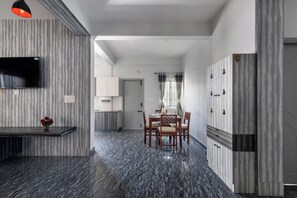 A modern kitchen with a flat-screen TV, a dining area with a table and chairs, and a hallway leading to a bedroom. - Indigo Studio by Jadecaps 1bhk New Town Kolkata (Barasat)