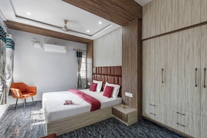 A modern bedroom with a bed, a chair, a wardrobe, and a ceiling fan. - Indigo Studio by Jadecaps 1bhk New Town Kolkata (Barasat)
