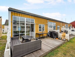 A modern, single-story building with large glass windows, a wooden deck, and outdoor furniture. - 4 Star Holiday Home in Ebeltoft (Pandrup)