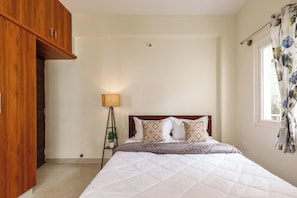 Quarto com cama, guarda-roupa de madeira, luminária de cabeceira e janela com cortinas.