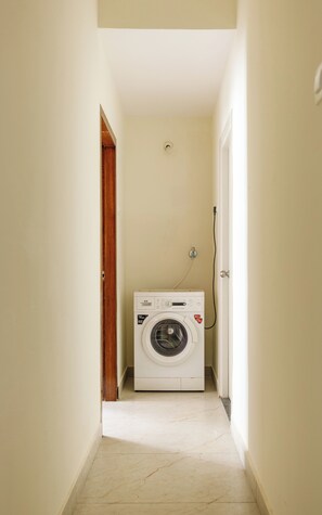 Uma lavanderia com uma máquina de lavar, uma porta e um interruptor de luz na parede.